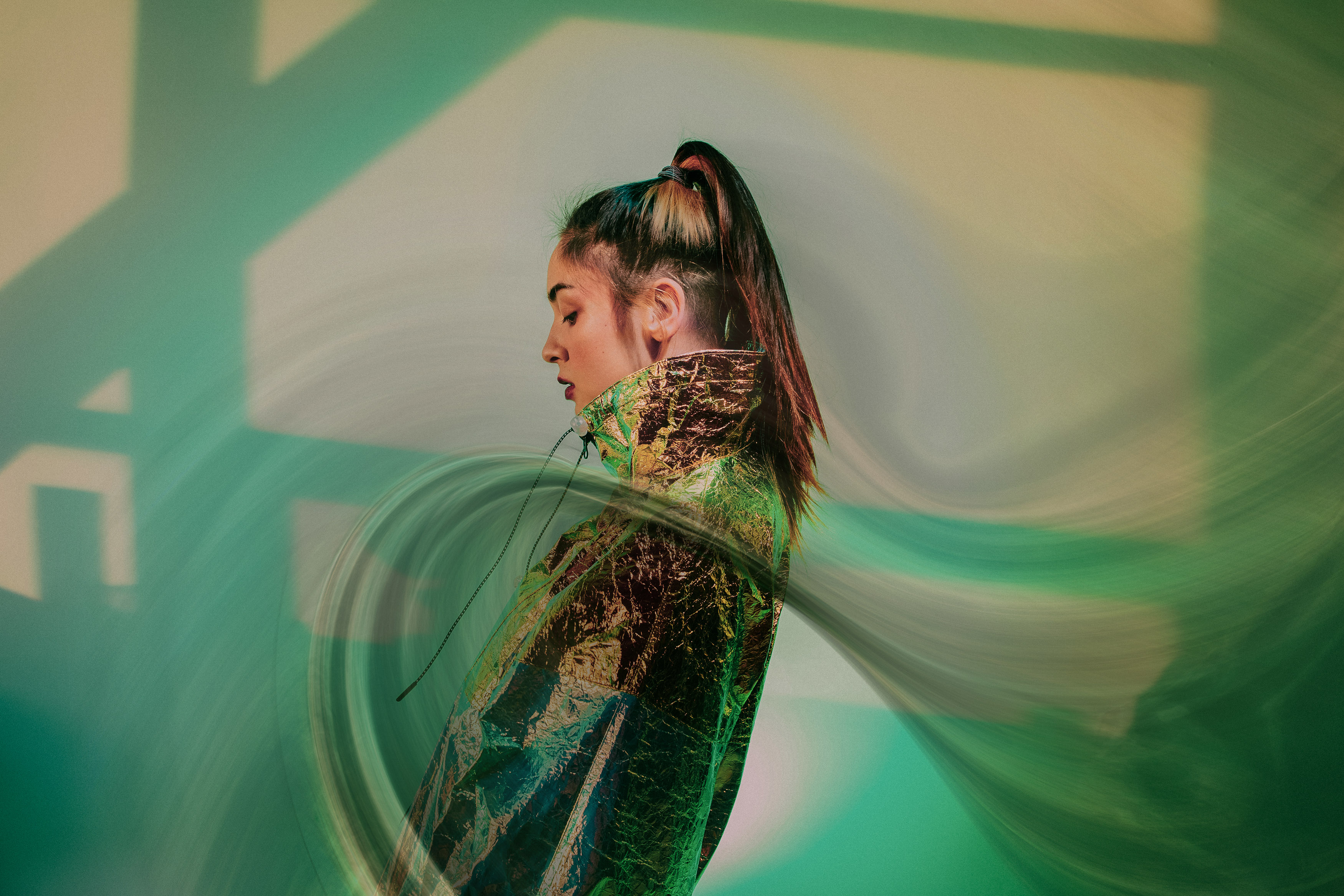 Woman in metallic jacket with abstract green and gold background.